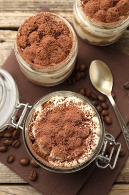 Kavanozlarda nefis tiramisu, kahve çekirdekleri ve kaşıklar masada, düz yerde.