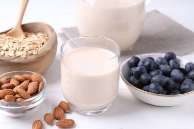 Badem sütü, yulaf ezmesi, fındık ve yaban mersini beyaz ahşap masada, yakın plan.