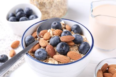 Yulaf gevreği, badem sütü, yaban mersini ve fındık beyaz masada, yakın plan.