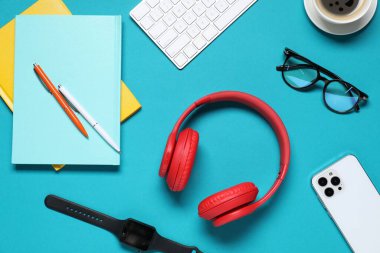 Açık mavi arkaplan üzerinde kulaklık ve kırtasiye ile düz kompozisyon yatıyordu