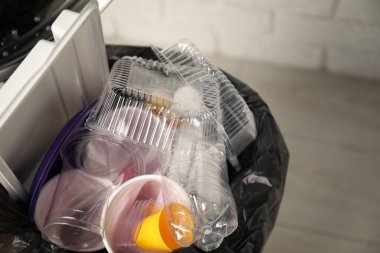 Plastic packaging in trash bin indoors, closeup. Space for text