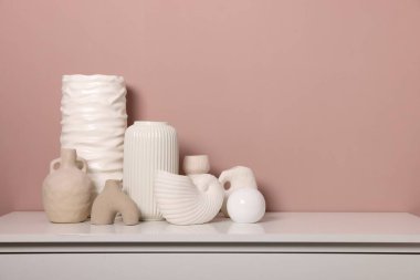 Koyu bej duvarın yanındaki dolapta farklı güzel vazolar var.