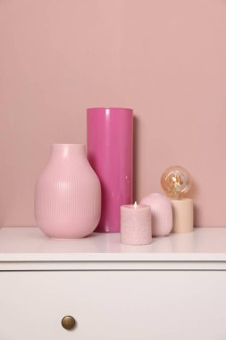Farklı güzel vazolar, yanan mum ve lamba, kapalı alandaki bej duvarın yanındaki dolapta.