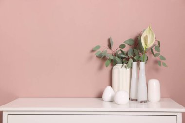 Bej duvarın yanındaki dolapta çiçek dekoru olan farklı güzel vazolar.