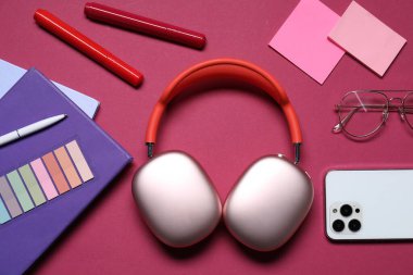Kulaklıklar, akıllı telefon, kırtasiye malzemeleri ve kırmızı arka planda gözlük, düz konum