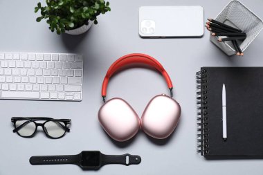Kulaklıklar, bilgisayar klavyesi, akıllı saat, akıllı telefon, kırtasiye, gözlük ve çiçek dekoru açık gri arka planda, düz konum
