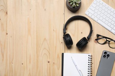 Kulaklıklar, akıllı telefon, bilgisayar klavyesi, gözlükler, kırtasiye malzemeleri ve ahşap masa üzerindeki çiçek dekoru, düz yatak. Metin için boşluk