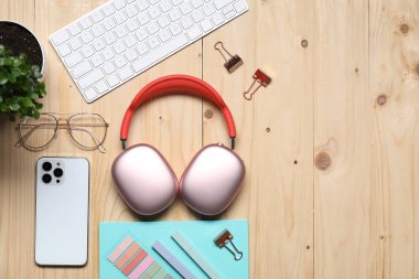 Kulaklıklar, akıllı telefon, bilgisayar klavyesi, gözlükler, kırtasiye malzemeleri ve ahşap masa üzerindeki çiçek dekoru, düz yatak. Metin için boşluk