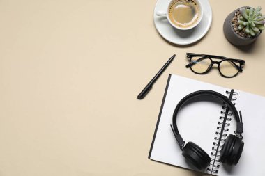 Kulaklıklar, bardaklar, kahve, çiçek dekoru ve bej arka planda kırtasiye malzemesi, düz yatak. Metin için boşluk
