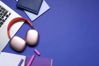 Kulaklıklar, dizüstü bilgisayarlar ve mavi arka planda kırtasiye malzemesi. Metin için boşluk