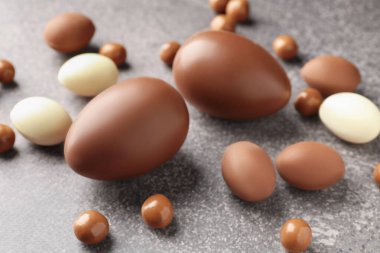 Paskalya kutlaması. Gri desenli masada bir sürü çikolata yumurtası ve dragee, yakın plan.