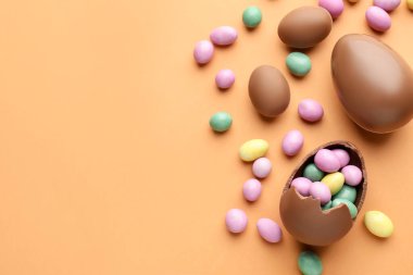 Soluk turuncu arka planda çikolatalı Paskalya yumurtaları ve şekerler. Metin için boşluk