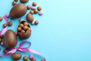 Çikolatalı Paskalya yumurtaları ve açık mavi arka planda menekşe kurdelesi. Metin için boşluk