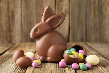 Çikolatalı tavşan ve renkli şekerli yumurtalar ahşap masada, yakın plan. Mutlu Paskalyalar