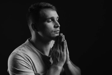 Genç adam karanlık arka planda dua ediyor, mesaj için yer var. Siyah ve beyaz etkisi