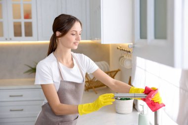 Evinde mikrofiber bezle mutfak musluğunu temizleyen kadın.