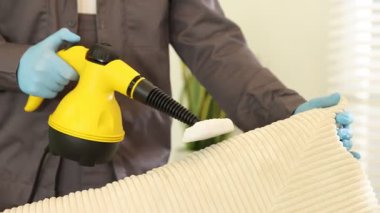 Haşere kontrol işçisi kanepeyi temizliyor. Kapalı alanda buhar temizleyicisi var.