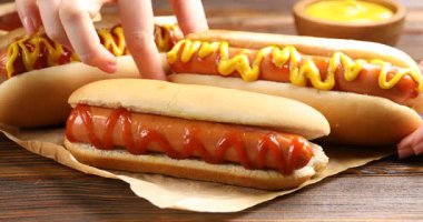 Ahşap masada hardallı lezzetli sosisli sandviç yiyen bir kadın.