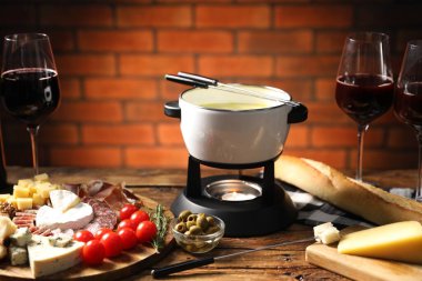 Kapalı masa üzerinde erimiş peynir, şarap ve atıştırmalıklarla fondü tenceresi (caquelon), yakın plan
