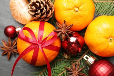 Köknar ağacı dalları, koniler ve siyah masanın üstünde Noel topları olan mandalinalar.