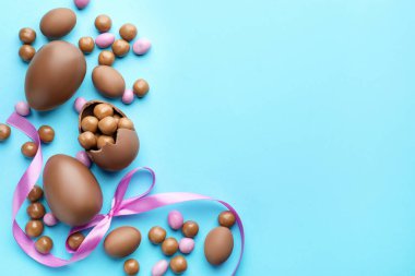 Çikolatalı Paskalya yumurtaları ve açık mavi arka planda menekşe kurdelesi. Metin için boşluk