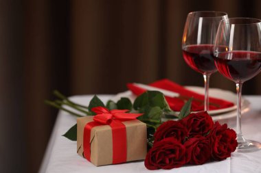 Şarap kadehleri, hediyeler ve kırmızı güllerle dolu güzel bir masa.
