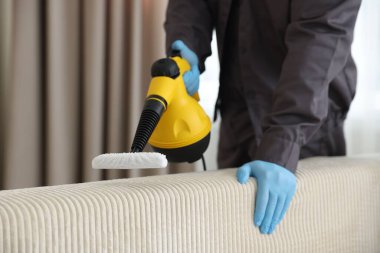 Haşere kontrol görevlisi kanepeyi temizliyor, kapalı alanda buharlı temizleyici ile, yakın plan. Metin için boşluk