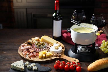 Nefis eritilmiş peynir fondü kabında, abur cuburlar ve bir şişe şarap ahşap masada, karanlık arka planda, yakın planda