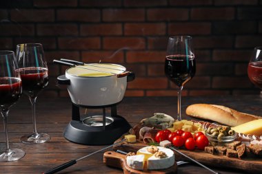 Kapalı masa üzerinde eritilmiş peynir, şarap ve atıştırmalıklar ile fondü tenceresi (caquelon)