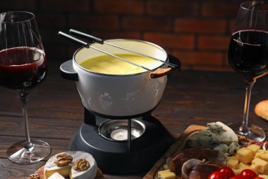 Erimiş peynir, şarap ve abur cuburla fondü tenceresi (caquelon), yakın plan.