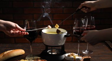 Kadınlar farklı aperatifleri fondü tenceresine (caquelon) daldırıyor. Eritilmiş peynirle kapalı masa içinde, yakın plan.