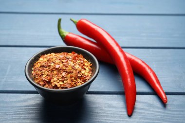 Kırmızı biber ve tanecikler mavi ahşap masada, yakın plan.