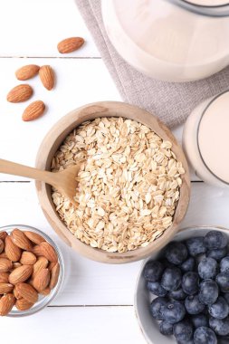 Badem sütü, yulaf ezmesi, fındık ve yaban mersini beyaz ahşap masa, düz uzanmış