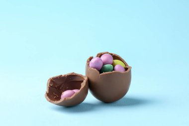 Kırık çikolata yumurtası ve açık mavi arka planda renkli şekerler. Mutlu Paskalyalar