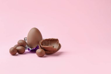 Tam ve kırılmış çikolata yumurtaları pembe arka planda, mesaj için yer var. Mutlu Paskalyalar