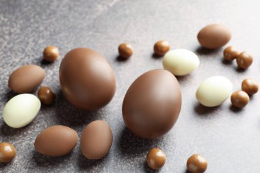 Paskalya kutlaması. Gri desenli masada bir sürü çikolata yumurtası ve dragee, yakın plan.