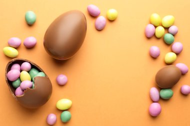 Soluk turuncu arka planda çikolatalı Paskalya yumurtaları ve şekerler. Metin için boşluk