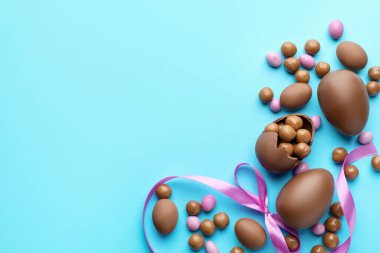 Çikolatalı Paskalya yumurtaları ve açık mavi arka planda menekşe kurdelesi. Metin için boşluk