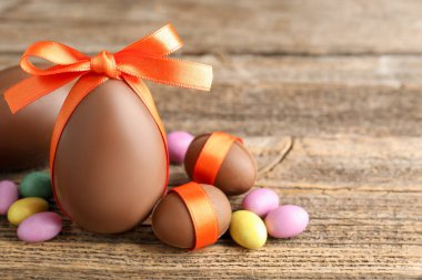 Mutlu Paskalyalar. Ahşap masada renkli şekerlemeli lezzetli çikolata yumurtaları, yakın plan. Metin için boşluk