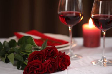 Şarap kadehleri, yanan mumlar ve kapalı alanda kırmızı güllerle güzel bir masa.