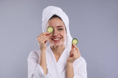 Havluya sarılı güzel bir kadın ve gri arka planda salatalık dilimleri.