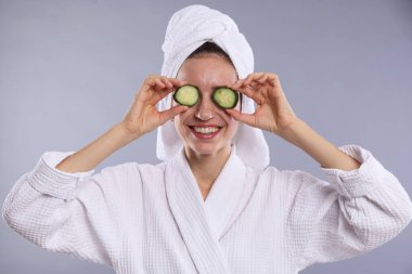 Havluya sarılı güzel bir kadın ve gri arka planda salatalık dilimleri.