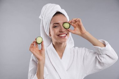 Havluya sarılı güzel bir kadın ve gri arka planda salatalık dilimleri.