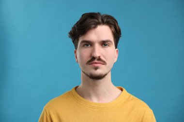 Açık mavi arka planda bıyıklı yakışıklı bir adam.