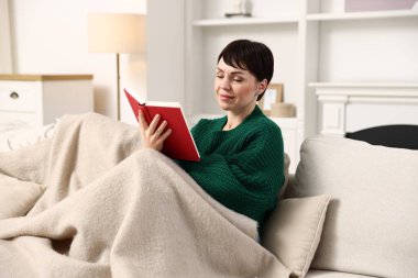 Evdeki kanepede kitap okuyan kadın.