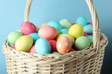 Açık mavi arka planda sepette güzel dekore edilmiş Paskalya yumurtaları, yakın plan.