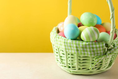 Beyaz masadaki sepetteki güzel Paskalya yumurtaları sarı arka planda, yakın plan. Metin için boşluk
