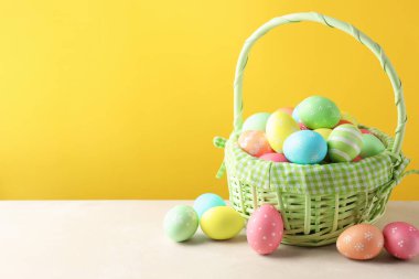 Beyaz masada sarı arka planda sepetteki güzel Paskalya yumurtaları. Metin için boşluk