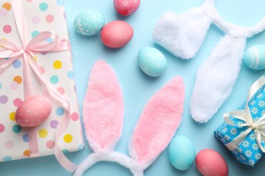 Mutlu Paskalyalar. Şirin tavşan kulakları, hediye kutuları ve açık mavi arka planda boyanmış yumurtalar, düz yatış.