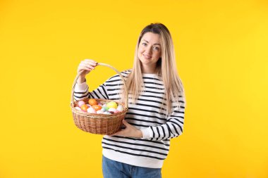 Paskalya kutlaması. Sarı arka planda boyanmış yumurta dolu sepeti olan gülümseyen kadın.